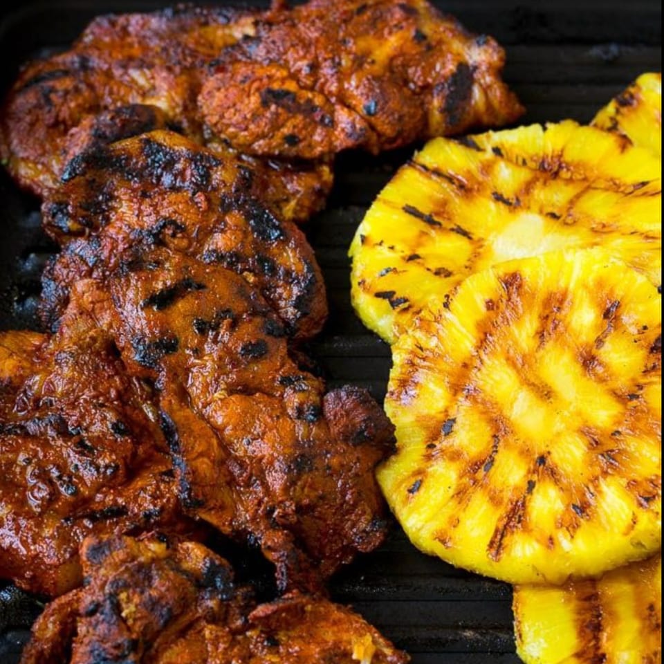 Grilled Mexican-style marinated chicken and pineapple slices cooking on a black grill.