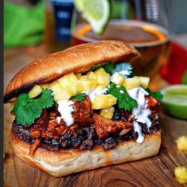 Mexican torta with pulled pork, black beans, pineapple, cilantro, and crema on a wooden board.