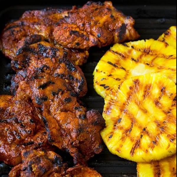 Grilled marinated pork and pineapple slices with char marks on a dark grill.
